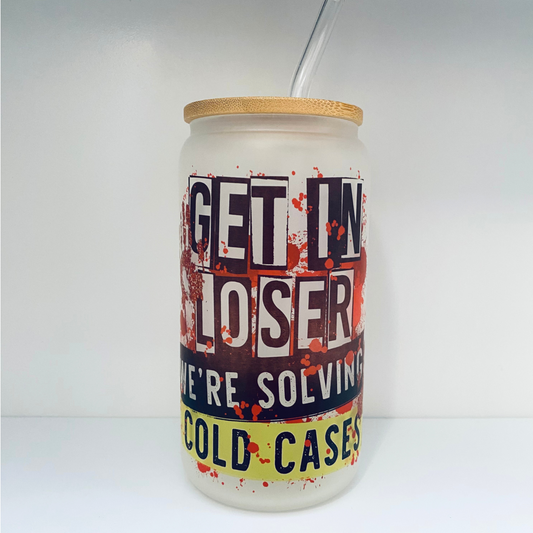 frosted glass cup with a bamboo lid and reusable straw. Glass cup has a "get in loser we're solving cold cases design